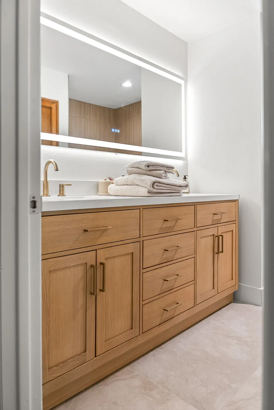 Vanity with a backlit mirror, light-wood cabinet and brass faucet