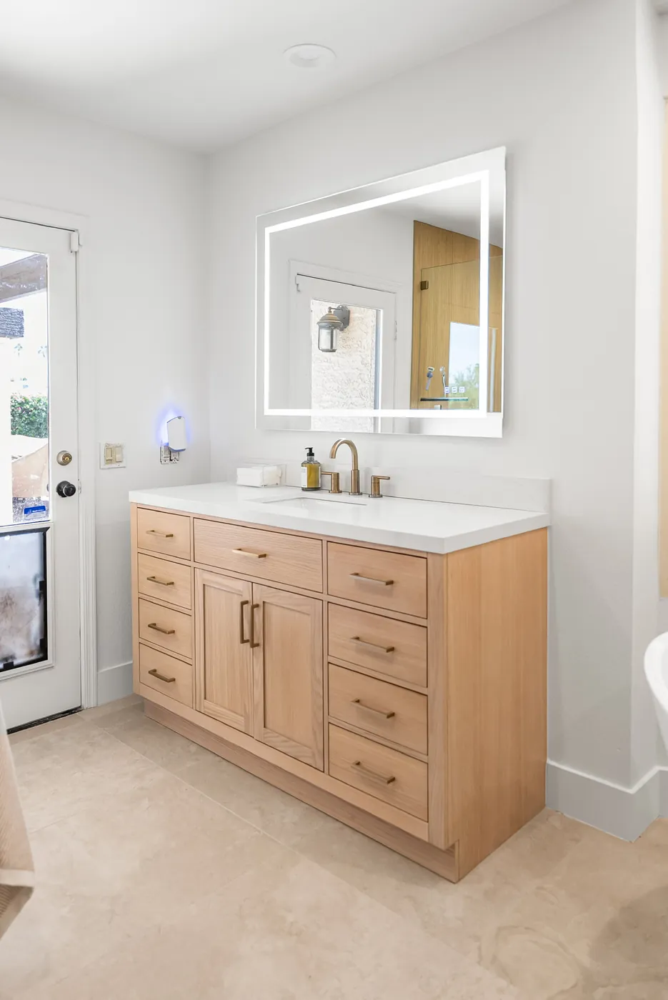 Second bathroom after: light-wood vanity, backlit mirror and brass faucet