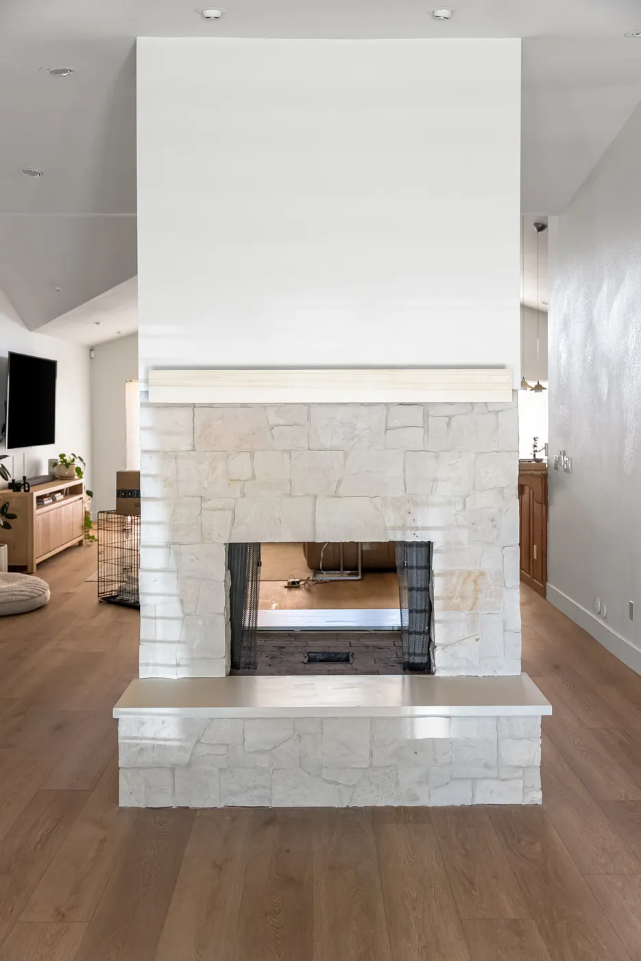 The fireplace after: refaced in stacked stone with a timber mantel, open to both rooms, on new wide-plank flooring