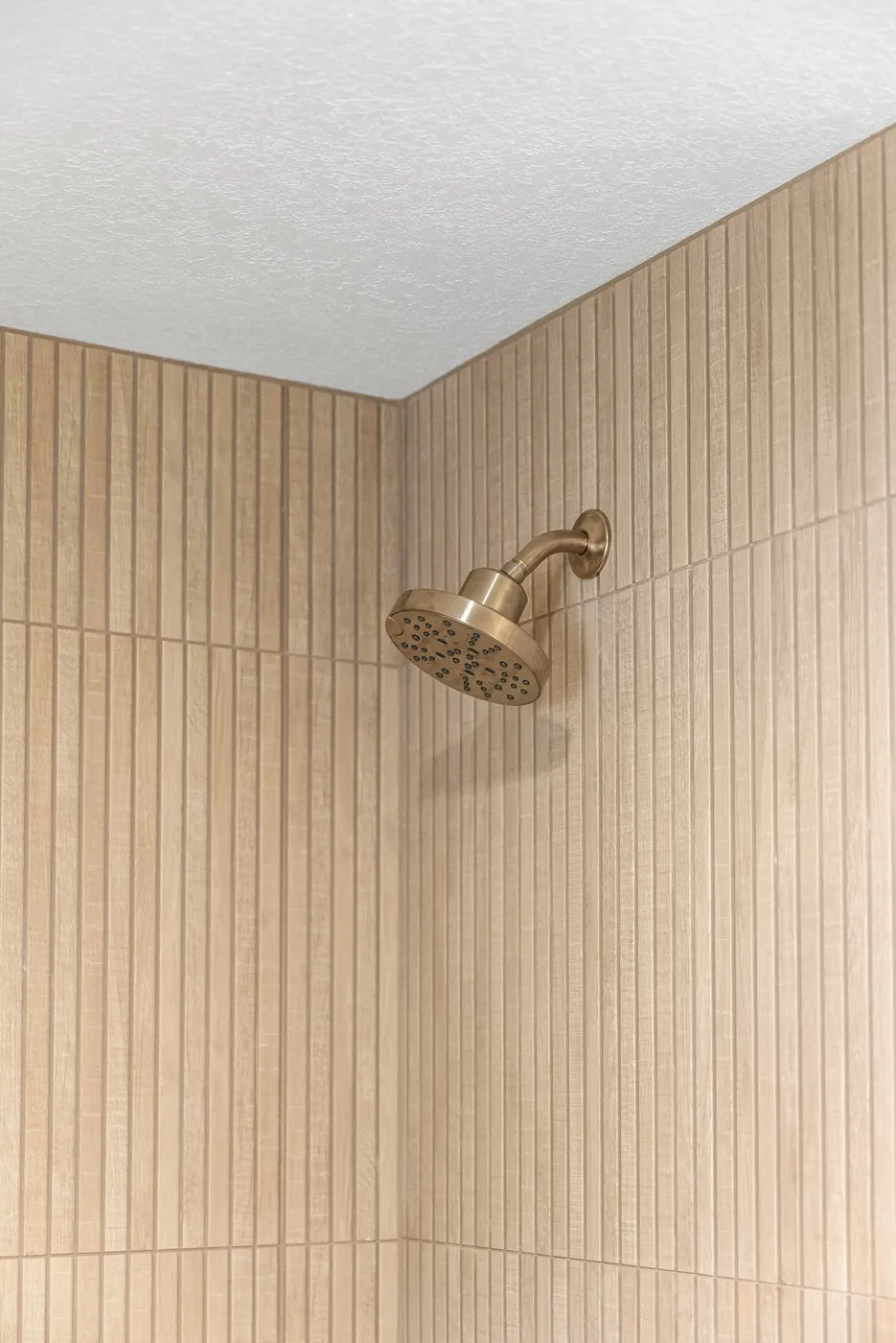 Brass shower head against the fluted tile