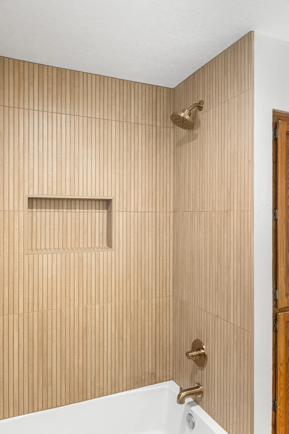 Tub surround in fluted wood-look tile with a recessed niche, brass fixtures and shower head