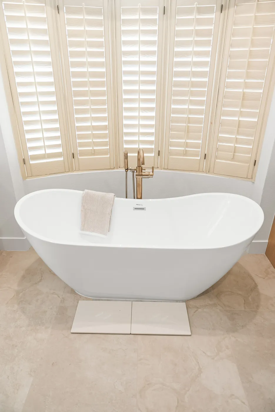Freestanding tub with a floor-mounted brass filler, shutters behind