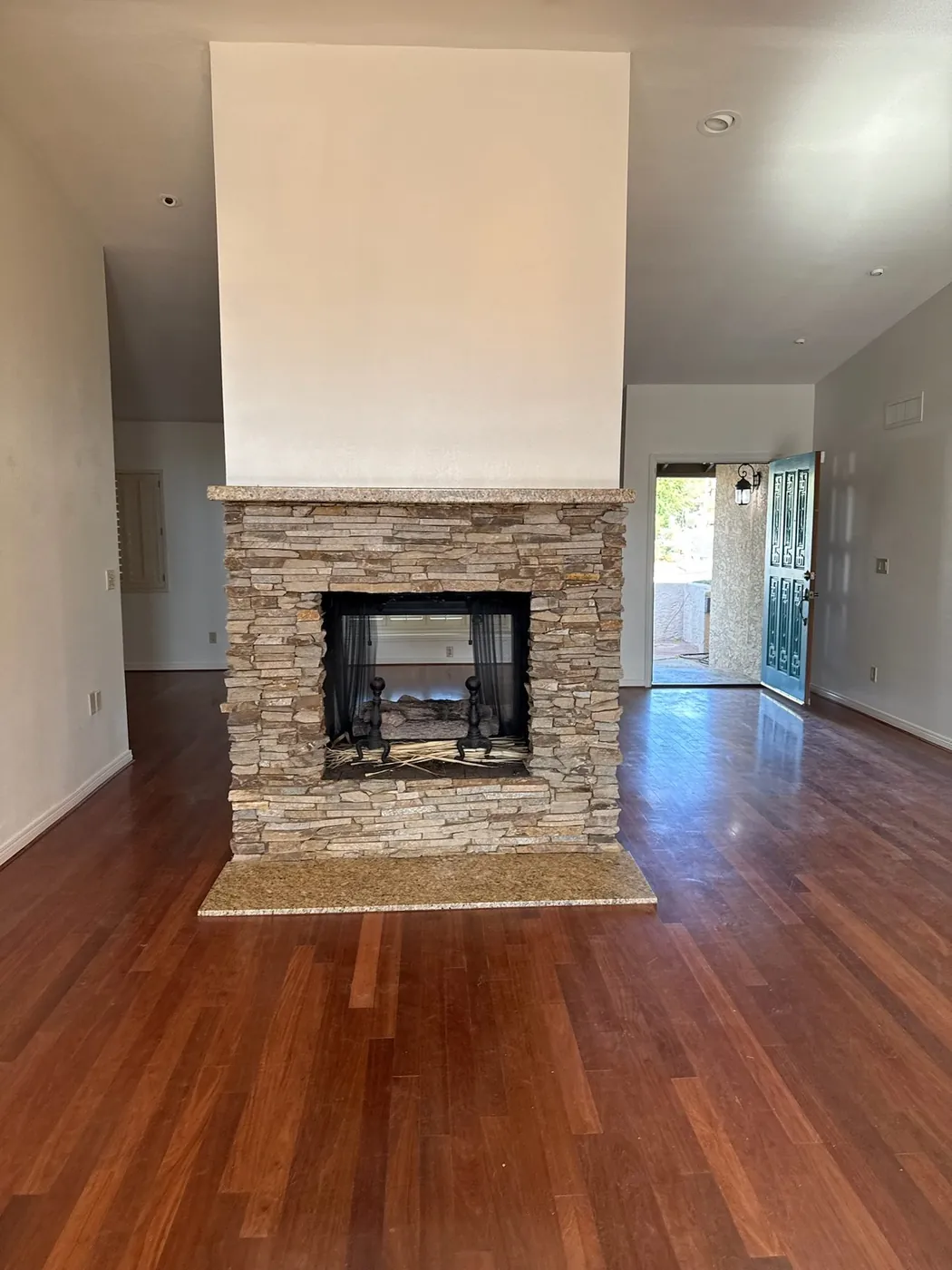 Living room side of the same fireplace before refacing, with the original stone base and cherry-toned flooring