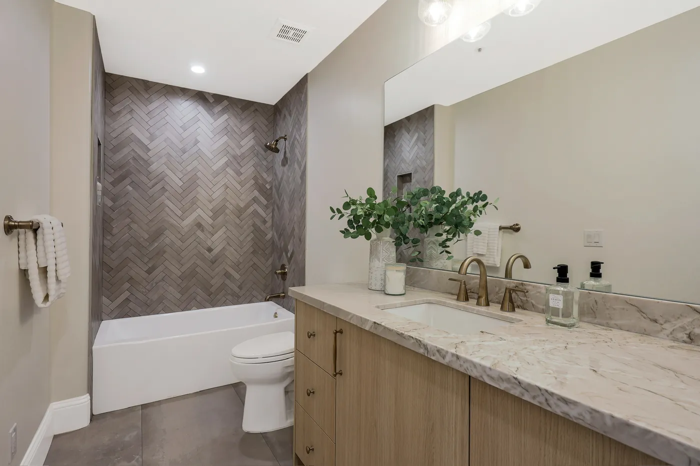 Bath with a herringbone-tiled tub surround and stone-topped vanity