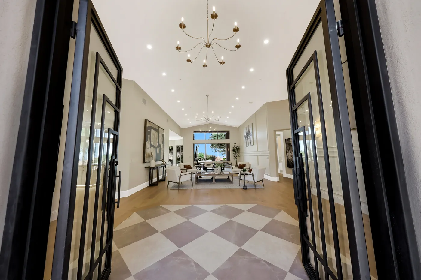 Entry through black steel pivot doors onto checkerboard tile, with the great room beyond