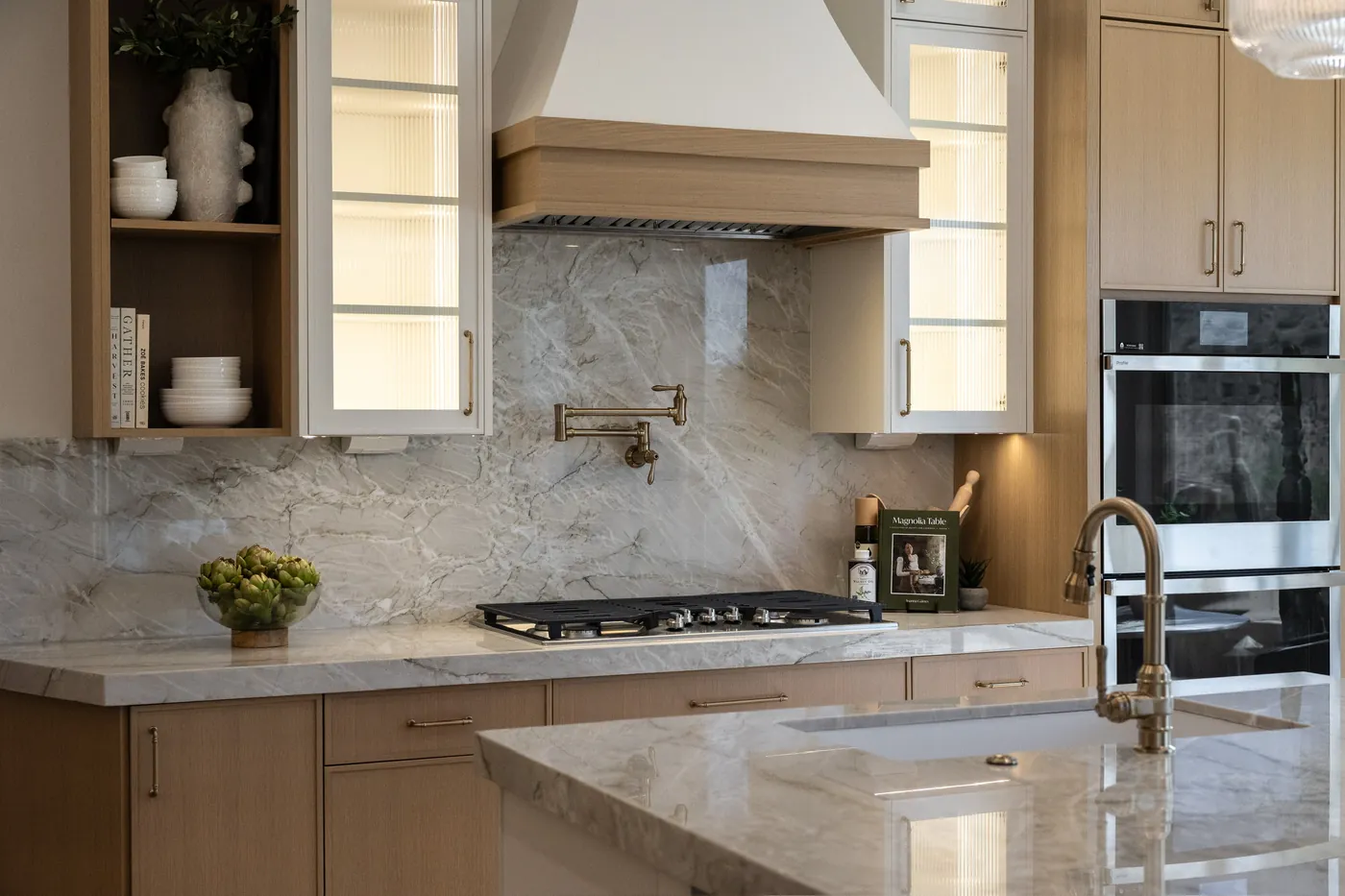 Range wall with a plaster hood, slab backsplash and lit glass-front uppers